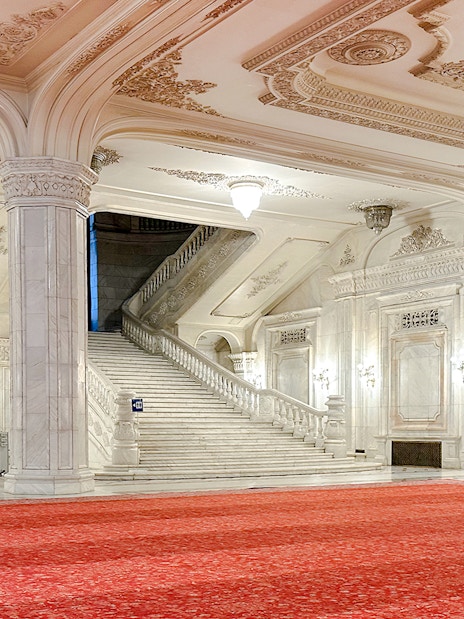 Grand staircase in the Palace of Parliament, Bucharest, with ornate ceilings and red carpet.