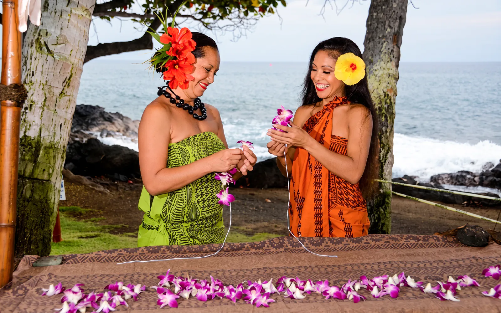 Lei making at Voyagers of the Pacific Luau with ocean backdrop.