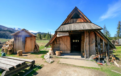 Bacowka Cheese Hut in a mountain meadow with wood stacks and clear sky.