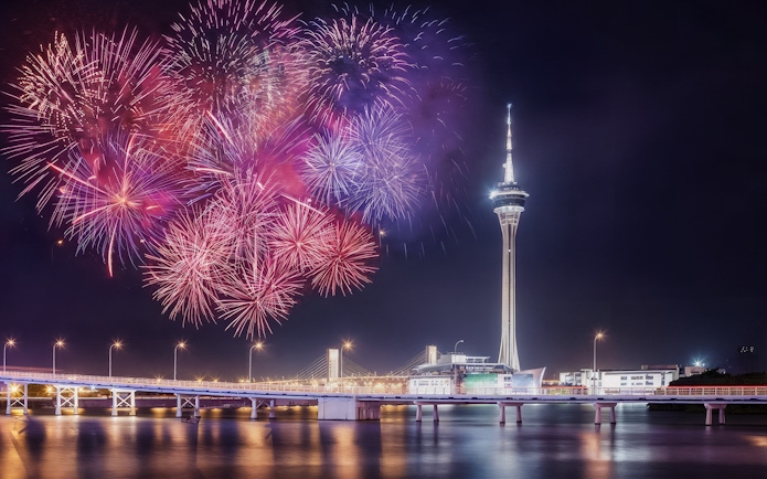 Fireworks over Hong Kong skyline viewed from TurboJET Ferry, featuring iconic tower and bridge.
