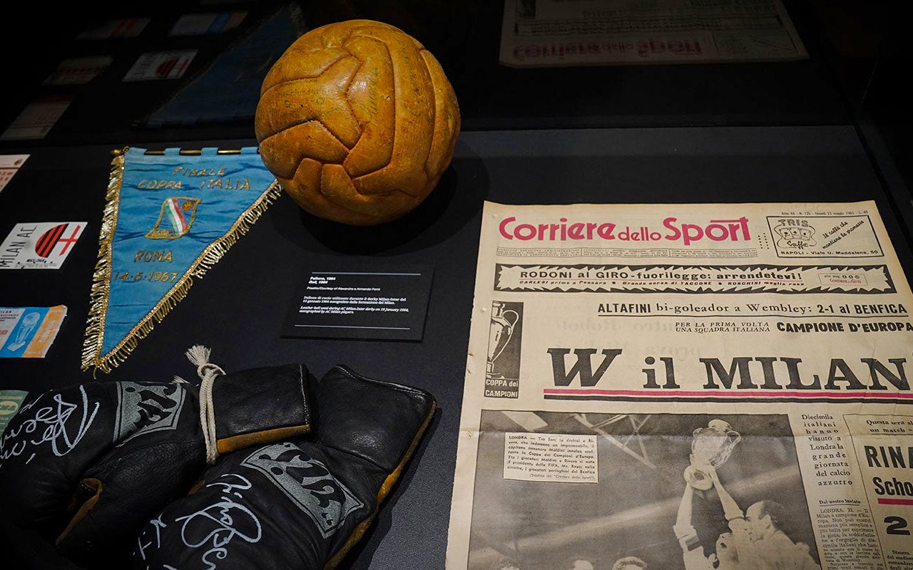 Casa Milan museum memorabilia display with vintage football, gloves, and Corriere dello Sport newspaper.