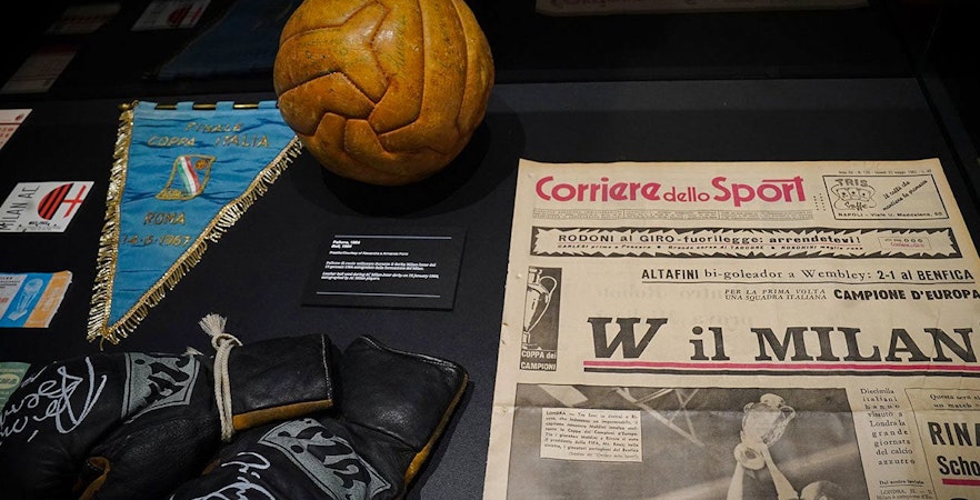 Casa Milan museum memorabilia display with vintage football, gloves, and Corriere dello Sport newspaper.