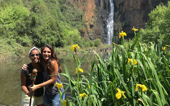 Visitors at a waterfall near the Mandela Capture Site, surrounded by lush greenery and yellow flowers.