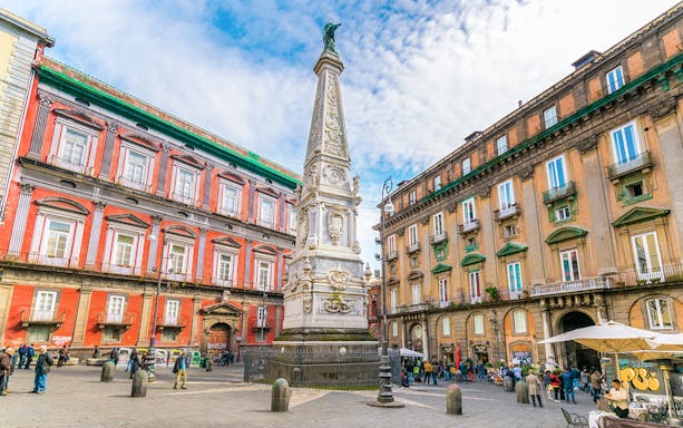 Obelisk of San Domenico in Naples surrounded by historic buildings and people.