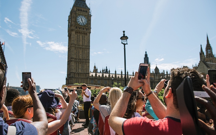 Tourists on a Big Bus near Big Ben in London, taking photos of the landmark.