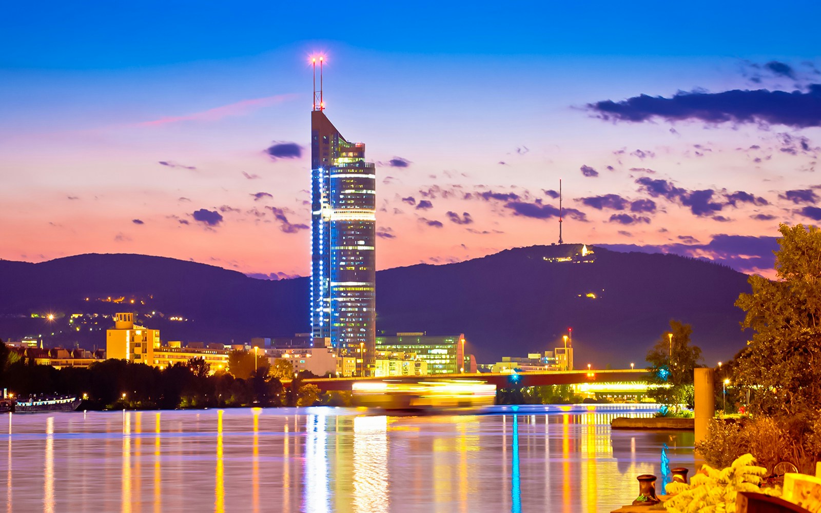 Aerial view of Vienna with skyscrapers, historic buildings, and riverside promenade at dusk.