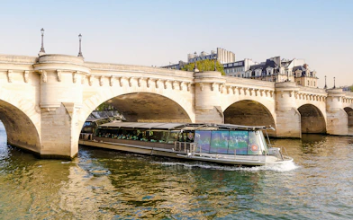 Bateaux Parisiens cruise boat passing under a stone bridge on the Seine River in Paris, France.