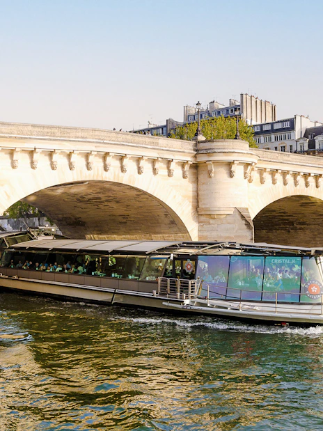 Bateaux Parisiens cruise boat passing under a stone bridge on the Seine River in Paris, France.
