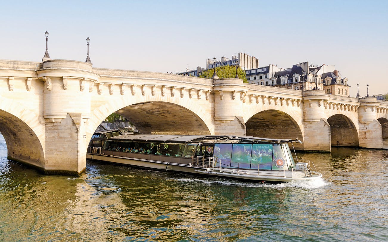 Bateaux Parisiens cruise boat passing under a stone bridge on the Seine River in Paris, France.