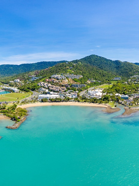 Aerial view of Airlie Beach and Whitsundays coastline with boats and lush hills.
