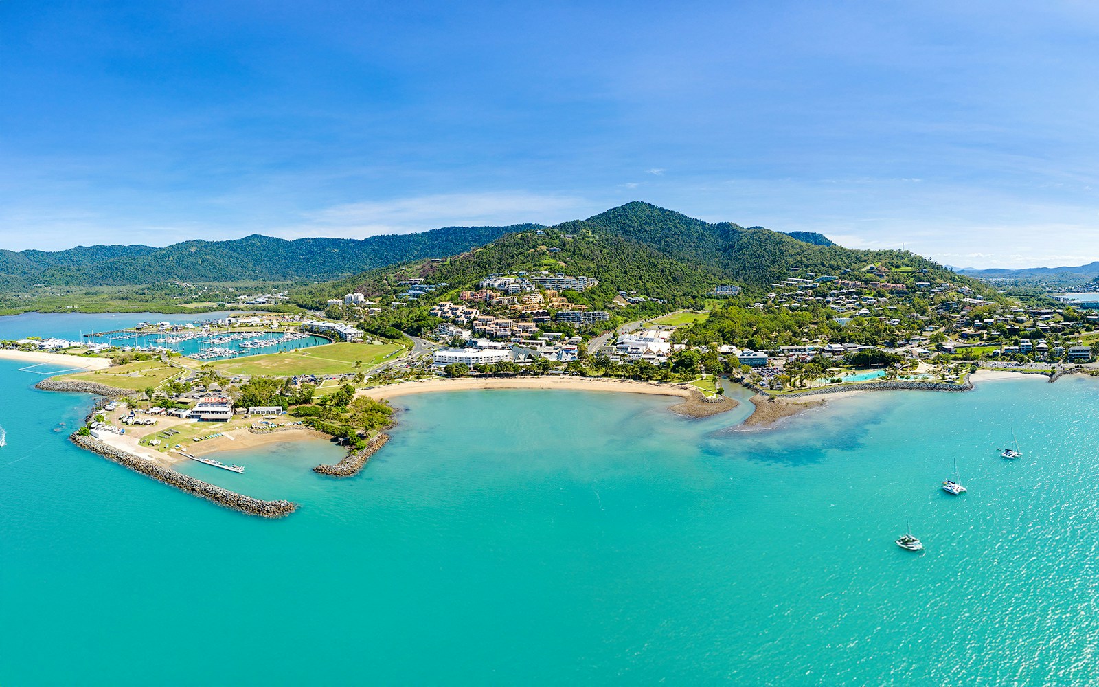Aerial view of Airlie Beach and Whitsundays coastline with boats and lush hills.