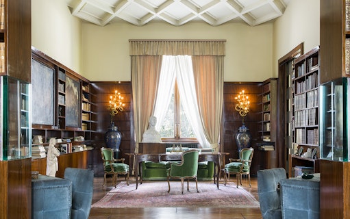 Villa Necchi Campiglio library with bookshelves, green chairs, and a bust on a desk.