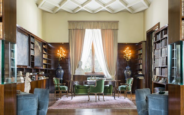 Villa Necchi Campiglio library with bookshelves, green chairs, and a bust on a desk.
