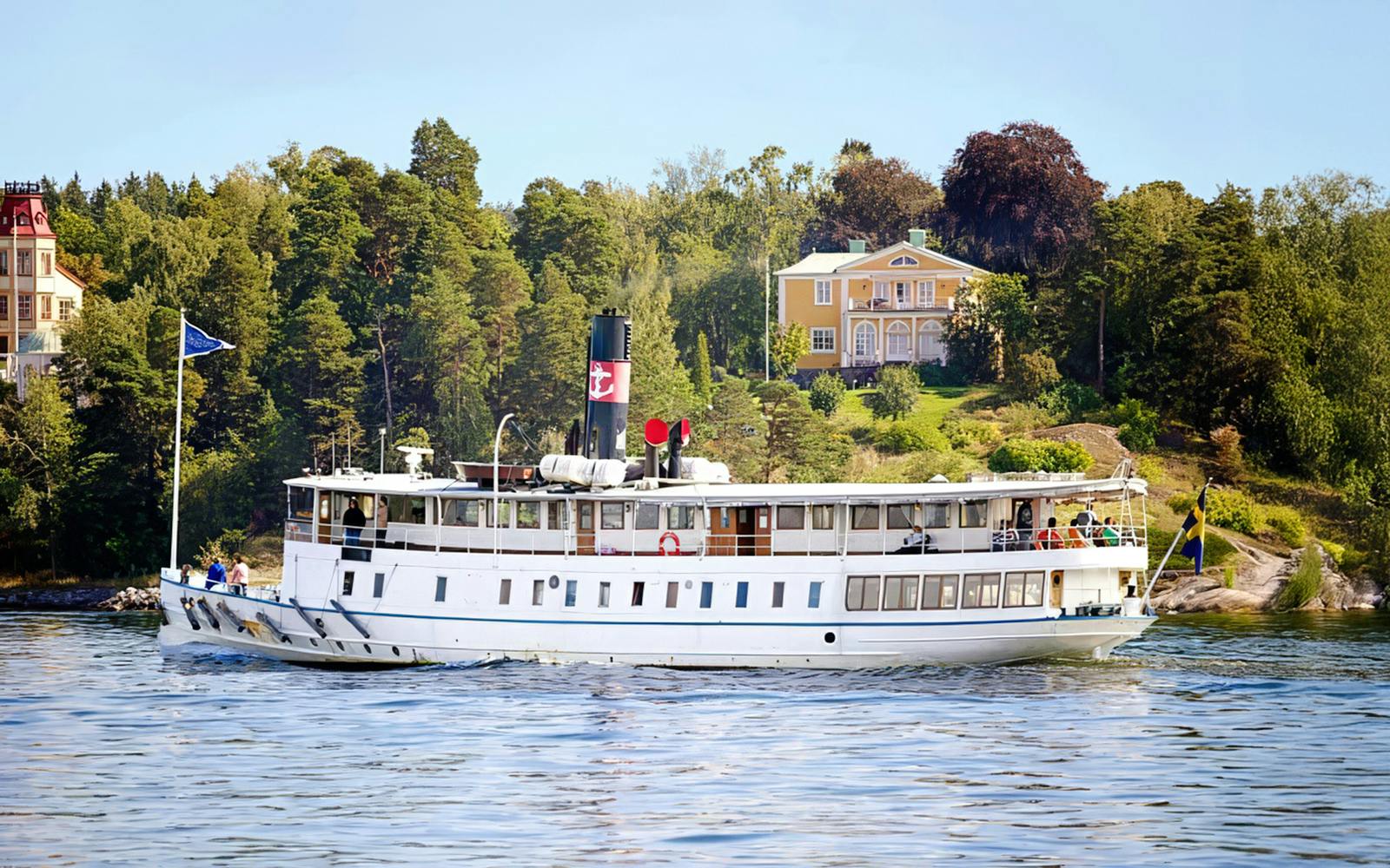 Cruise ship sailing through Stockholm archipelago with scenic coastal homes.