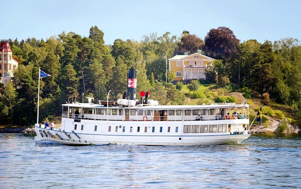 Cruise ship sailing through Stockholm archipelago with scenic coastal homes.