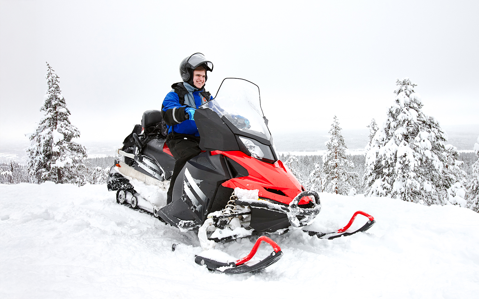 Man driving snowmobile through snowy forest in Lapland.