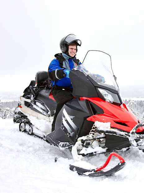 Man driving snowmobile through snowy forest in Lapland.