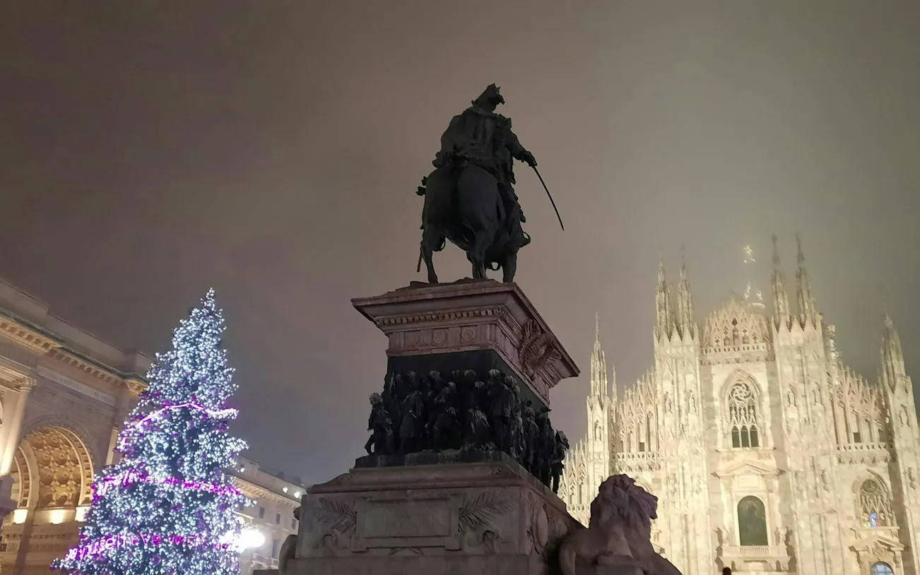 Equestrian statue and Christmas tree in front of Milan Cathedral at night.