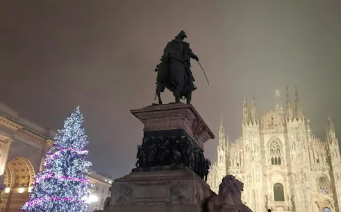 Equestrian statue and Christmas tree in front of Milan Cathedral at night.
