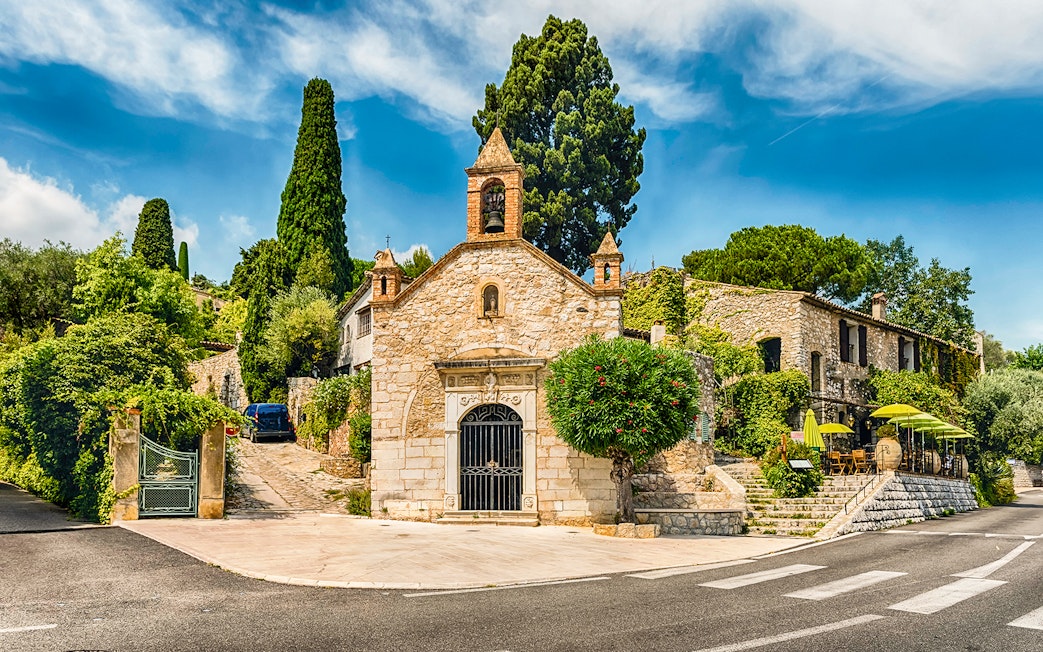 Stone chapel and cafe with green umbrellas on a French Riviera street, Nice day tour.