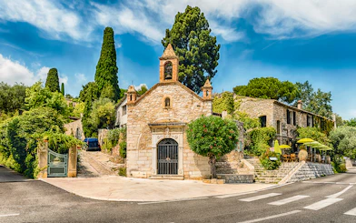 Stone chapel and cafe with green umbrellas on a French Riviera street, Nice day tour.