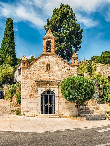 Stone chapel and cafe with green umbrellas on a French Riviera street, Nice day tour.