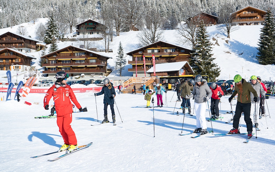 Beginner skiers learning on snowy slopes in Grindelwald with wooden chalets in the background.