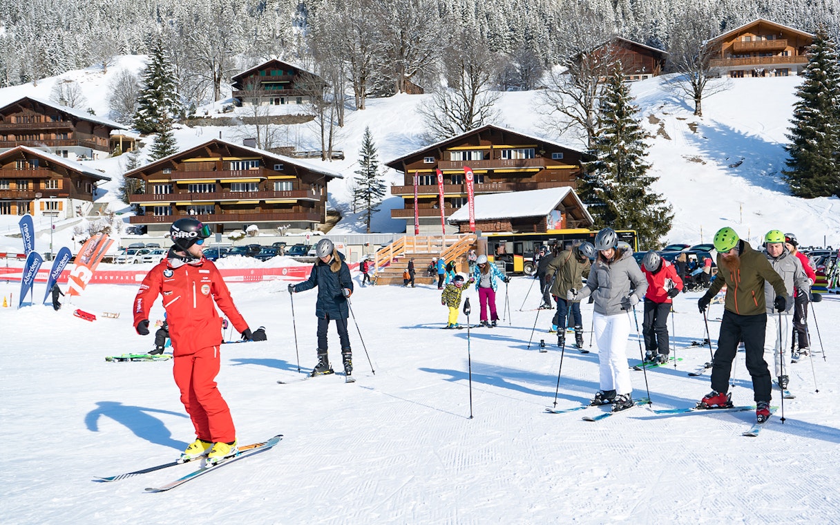 Beginner skiers learning on snowy slopes in Grindelwald with wooden chalets in the background.