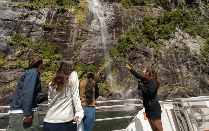 Tourists on a boat admire a waterfall at Milford Sound, New Zealand.