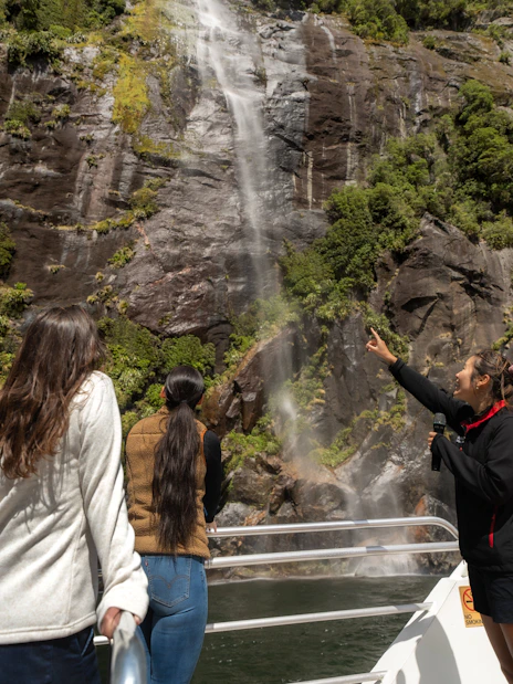 Tourists on a boat admire a waterfall at Milford Sound, New Zealand.