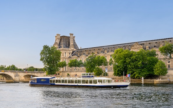 Dinner cruise boat on the Seine River passing by the Louvre Museum in Paris.