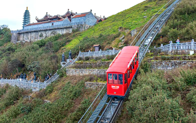 Red funicular ascending Fansipan Mountain with pagoda in background at Sun World Fansipan Legend, Vietnam.