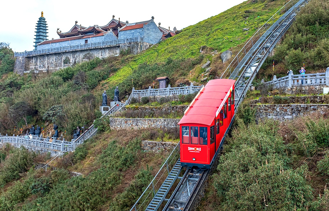 Red funicular ascending Fansipan Mountain with pagoda in background at Sun World Fansipan Legend, Vietnam.