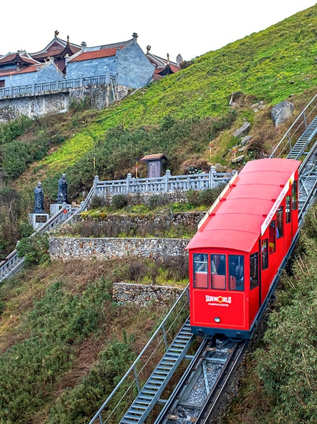 Red funicular ascending Fansipan Mountain with pagoda in background at Sun World Fansipan Legend, Vietnam.