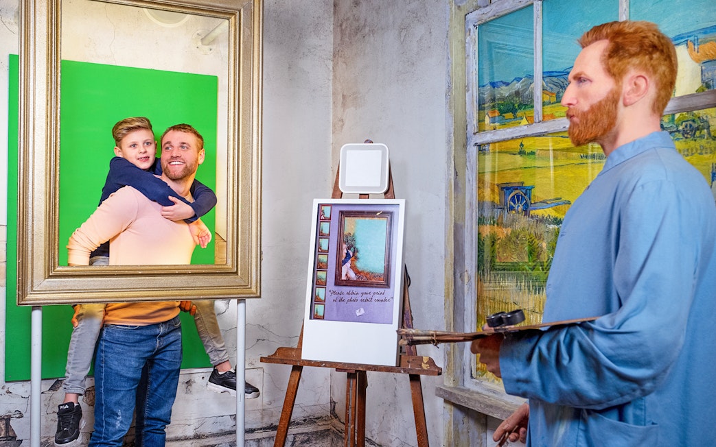 Man and child posing in frame with Vincent van Gogh figure at Madame Tussauds Amsterdam.