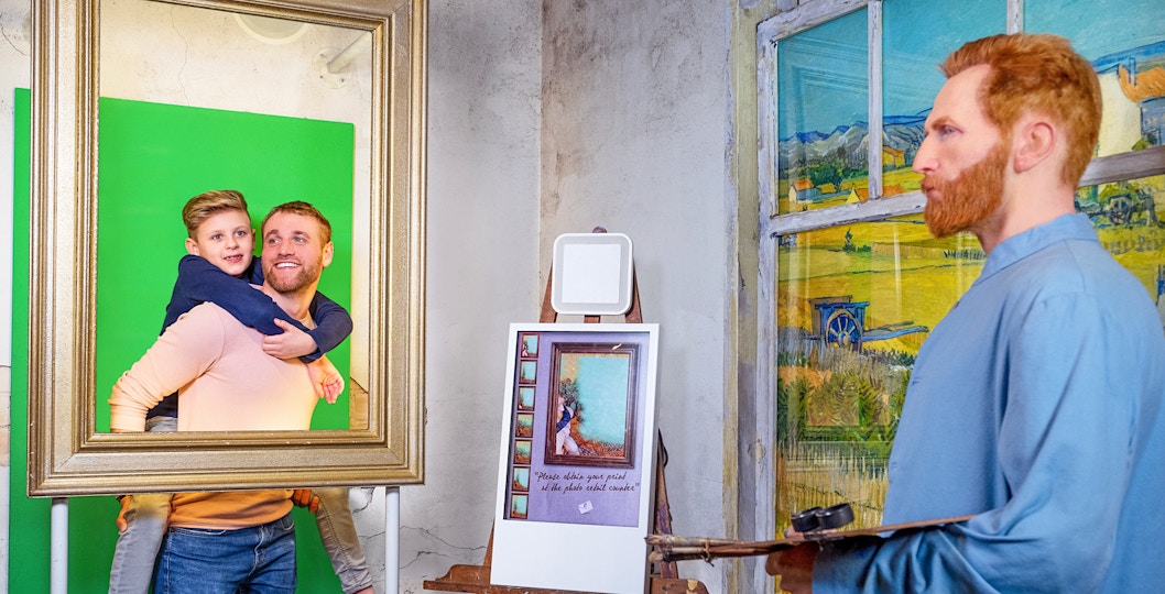 Man and child posing in frame with Vincent van Gogh figure at Madame Tussauds Amsterdam.