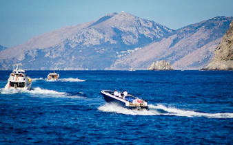 Speed boats cruising along the Amalfi Coast with mountainous backdrop.