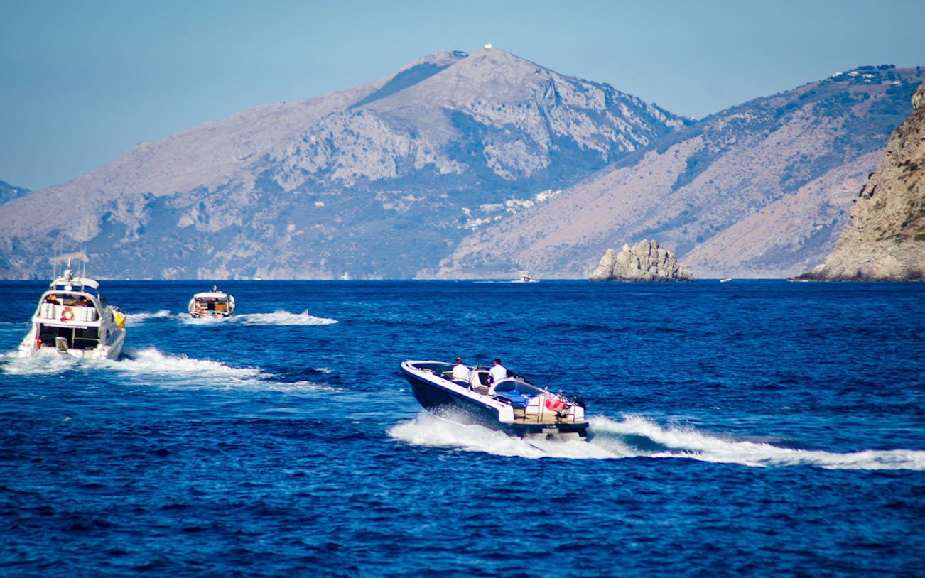 Speed boats cruising along the Amalfi Coast with mountainous backdrop.