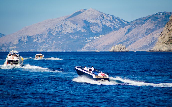 Speed boats cruising along the Amalfi Coast with mountainous backdrop.