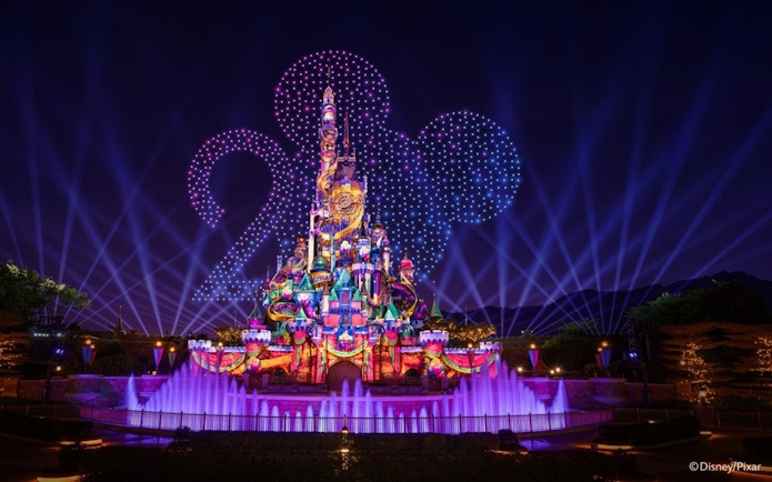 Disneyland Hong Kong castle illuminated with night lights for 20th anniversary celebration.