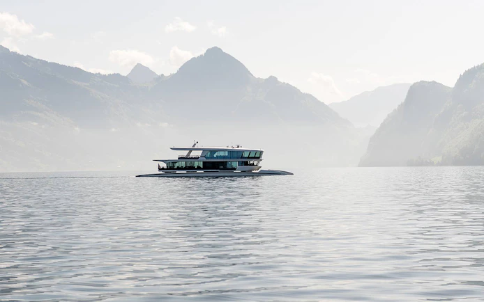 Catamaran cruising on a serene lake with mountain backdrop.