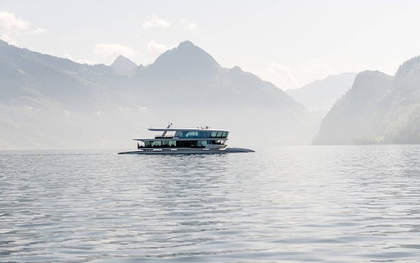 Catamaran cruising on a serene lake with mountain backdrop.
