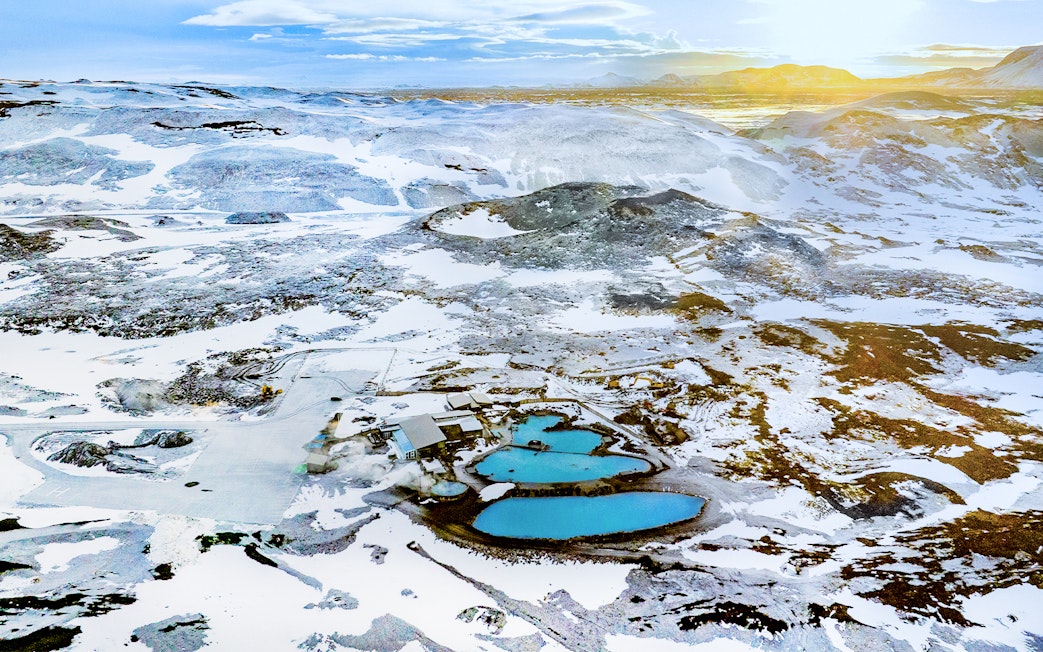 Aerial view of Myvatn Nature Baths hot spring surrounded by snow-covered landscape at sunrise, Iceland.