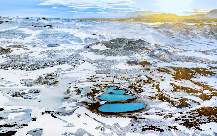 Aerial view of Myvatn Nature Baths hot spring surrounded by snow-covered landscape at sunrise, Iceland.