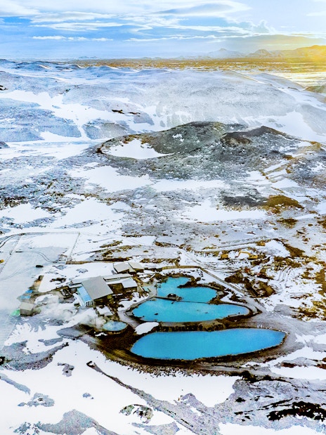 Aerial view of Myvatn Nature Baths hot spring surrounded by snow-covered landscape at sunrise, Iceland.