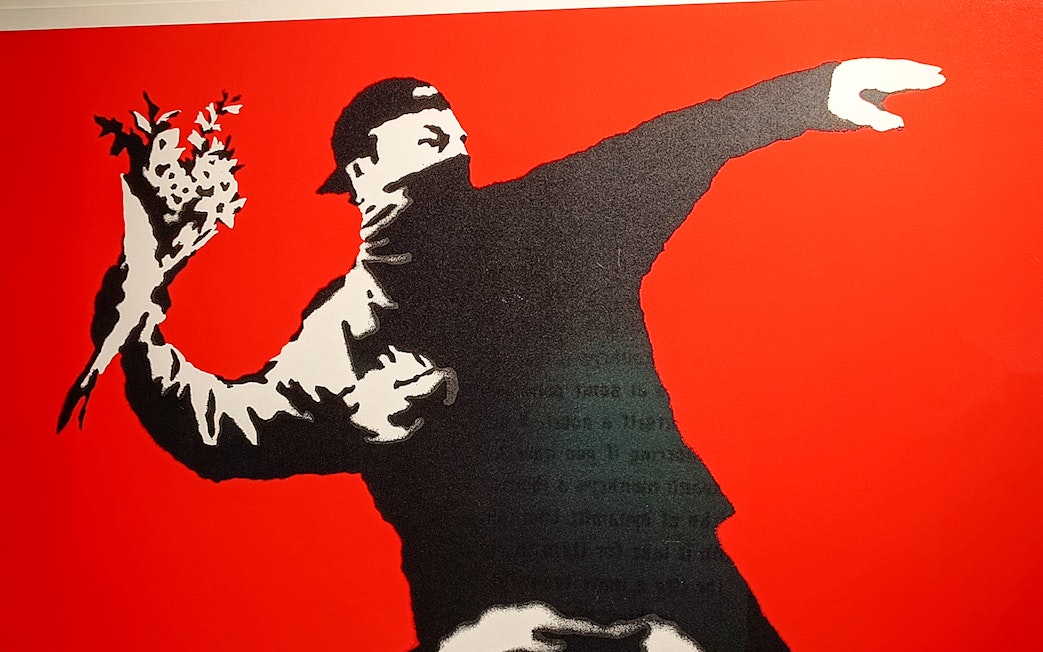 Street art of a masked figure throwing flowers, Banksy artwork.