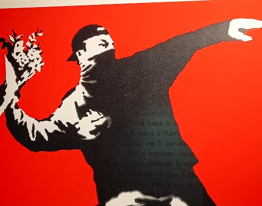 Street art of a masked figure throwing flowers, Banksy artwork.