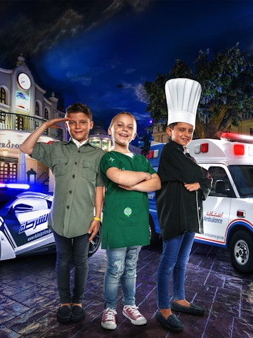 Children in costumes at KidZania Dubai, posing as a police officer, chef, and shopkeeper.