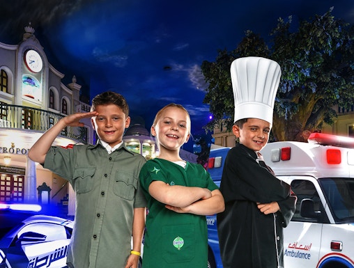 Children in costumes at KidZania Dubai, posing as a police officer, chef, and shopkeeper.