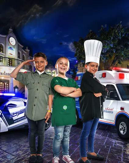 Children in costumes at KidZania Dubai, posing as a police officer, chef, and shopkeeper.